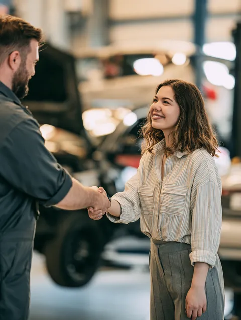 Transmission technician shaking hands with a woman in her 30s whose $2,000 loan paid for the repair on her lifted car.