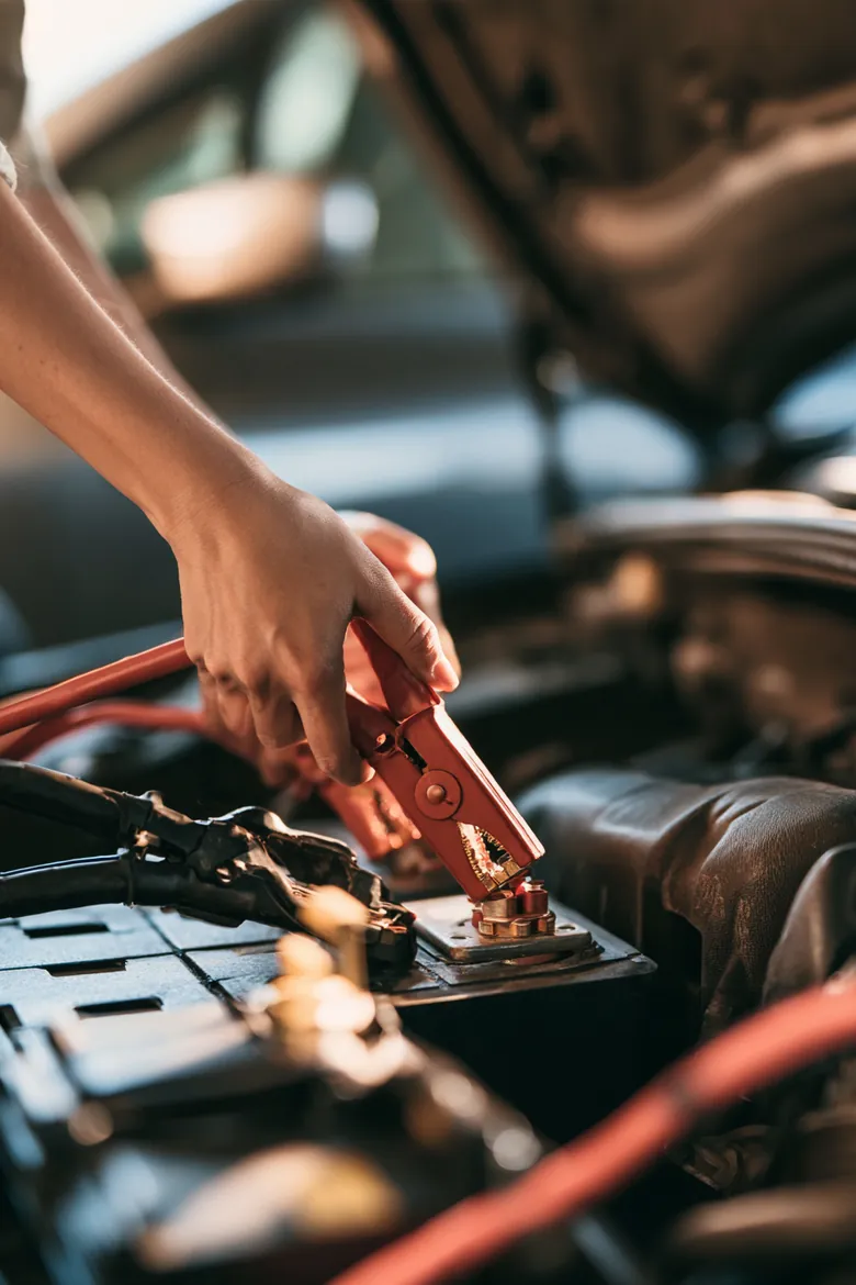 Close-up of a woman's hands clamping red jumper cables onto a battery terminal, an Auto Approve car cost guide image