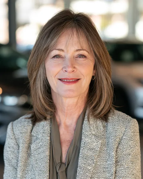 A smiling insurance agent in her 60s sits in a bright modern office, ready to help with a car insurance question.