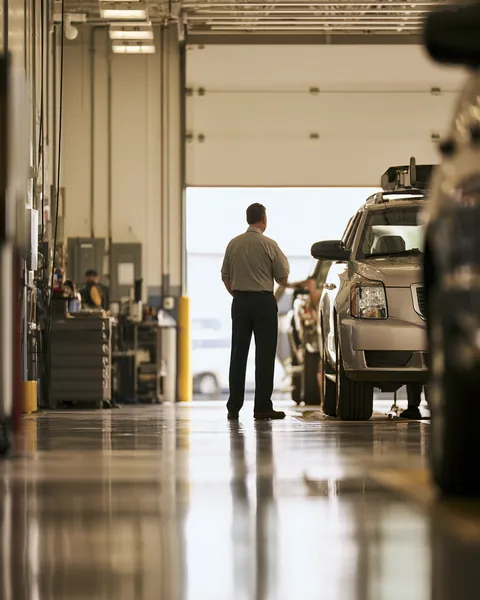 A technician checks an SUV in a bright state inspection lane while its owner, a man in his 50s, watches.