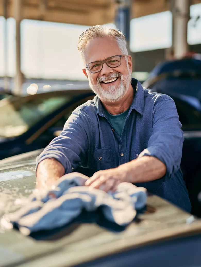 Man in his 50s smiling while drying his car hood at a car wash, featured in an Auto Approve funding guide