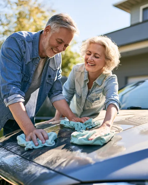 Couple in their 60s polishing the hood of their sedan with microfiber cloths in their driveway